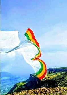 a rainbow colored kite is flying high in the sky on top of a rocky hill