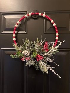 a wreath is hanging on the door with red and white beads, pine cones, and berries