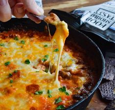 a person dipping cheese into a skillet with tortilla chips