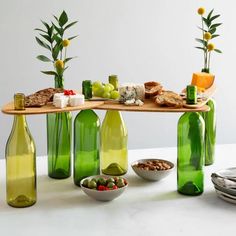 several green bottles with food in them on a table next to plates and bowls filled with fruit