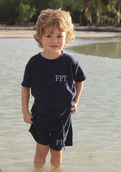 a little boy standing in the water at the beach with his hands on his hips