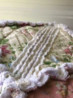 an old blanket with ruffles and flowers on it sitting on top of a bed