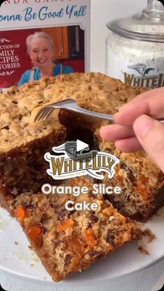 someone is cutting into an orange slice cake on a white plate with a book in the background