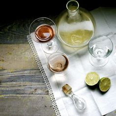 several glasses of wine and some lemons on a table with a white cloth next to them