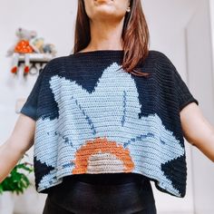 a woman with her hands in the air while wearing a crocheted top and black pants