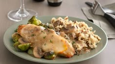 a plate with chicken and vegetables covered in gravy next to a glass of wine