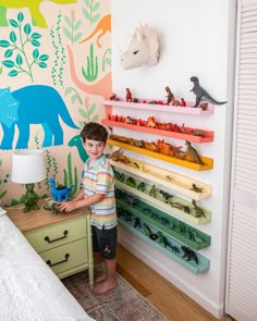 a little boy standing in front of a colorful wall with dinosaurs on it and toys