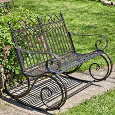 a metal bench sitting on top of a sidewalk next to some bushes and flowers in the grass