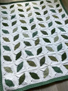 a green and white crocheted blanket with leaves on the bottom, sitting on a wooden floor