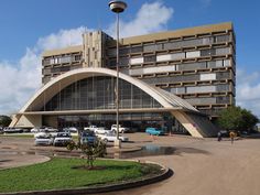 a large building with cars parked in front of it and people walking around the parking lot