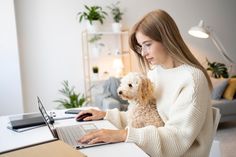 a woman sitting at a desk with her dog on her lap, working on a laptop