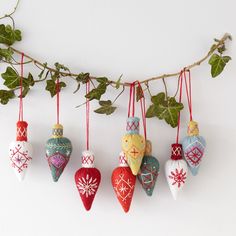 christmas ornaments hanging from a branch on a white wall