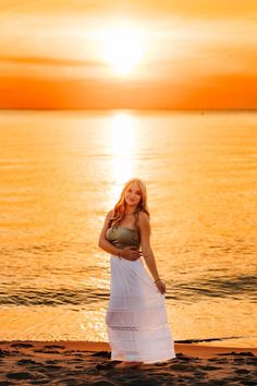 a woman standing on top of a beach next to the ocean in front of a sunset