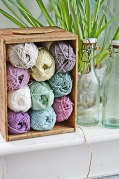 several balls of yarn are in a wooden box on a shelf next to a glass bottle