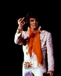 elvis presley performing on stage with an orange scarf around his neck and hands in the air