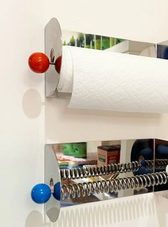 a toilet paper roll is hanging on the wall next to a mirror that has balls attached to it