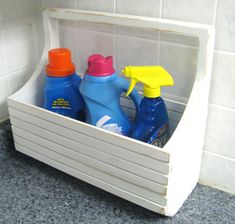 two spray bottles are sitting in a white container on the floor next to a tile wall