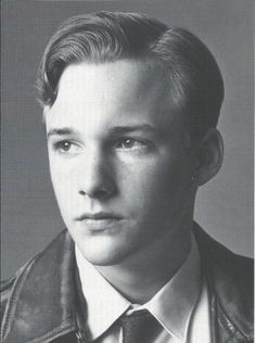 black and white photograph of a young man wearing a leather jacket, tie and dress shirt