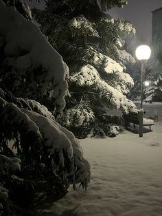 a park bench covered in snow next to a street light at night with the lights on