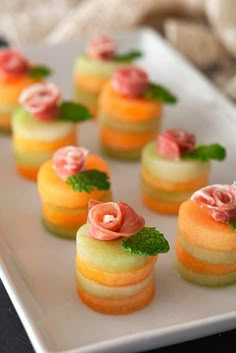 small desserts are arranged on a white plate with green leaves and pink flowers in the middle