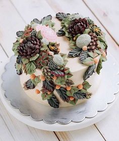 a white cake decorated with flowers and leaves on top of a platter in front of a wooden table