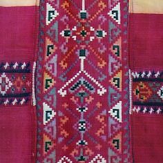 an old red rug with geometric designs on the bottom and sides, hanging from a wall