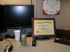 a desk with a computer monitor, cell phone and a framed award on top of it