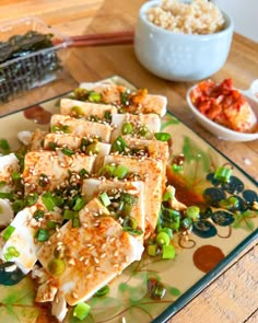 tofu with sesame seeds, peas and rice on a plate next to a bowl of sushi