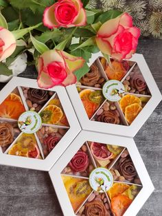 three white boxes filled with different types of candies next to pink roses and green leaves