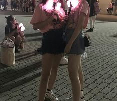 two young women standing next to each other in front of a building with lights on