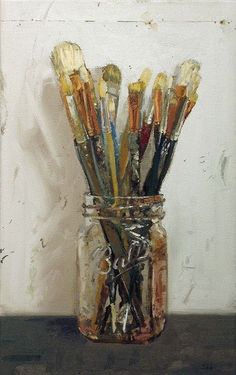 a jar filled with lots of paint brushes on top of a wooden table next to a white wall