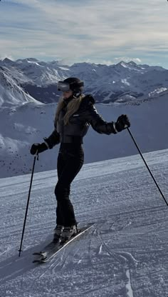 a woman riding skis down the side of a snow covered slope with mountains in the background