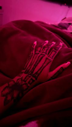 a woman's hand with tattoos on it laying in bed under a pink light