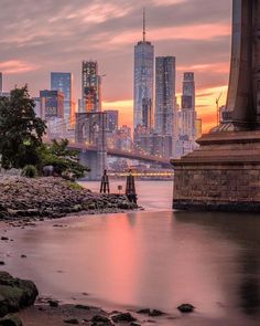 the city skyline is reflected in the water at sunset, with skyscrapers rising above