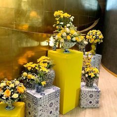 yellow and white flowers are in vases next to small boxes on the floor near a wall