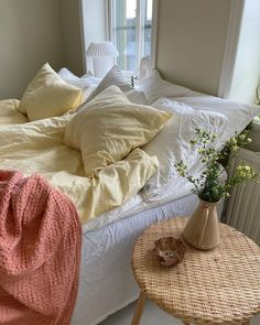 a bed that has some pillows on it and a table with flowers in front of it