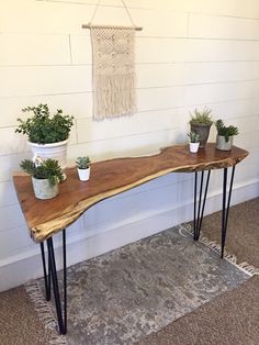 three potted plants sit on top of a wooden table with hairpin legs in front of a white wall