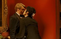 two men in tuxedos are kissing each other near a wall with a mirror