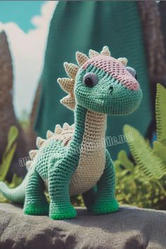 a crocheted dinosaur toy sitting on top of a rock