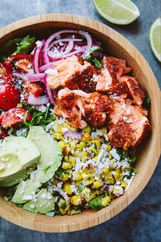 a wooden bowl filled with meat, vegetables and rice next to sliced lime wedges