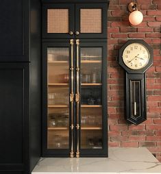 a clock mounted to the side of a brick wall next to a wine cabinet with glass doors