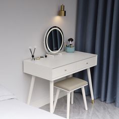 a white desk with a mirror and two stools in front of the window, next to a blue curtain