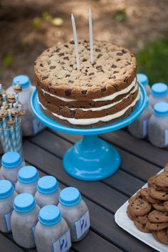 a cookie cake and cookies on a table with bottles of milk, candles and desserts