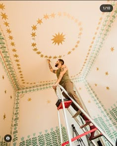 a man on a ladder painting a ceiling with star stencils in a room