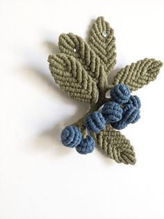 a crocheted brooch with blue flowers on it's end and green leaves