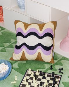 a pillow sitting on top of a green rug next to a chess board and game pieces