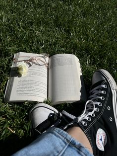 an open book sitting on top of a lush green field next to a person's legs