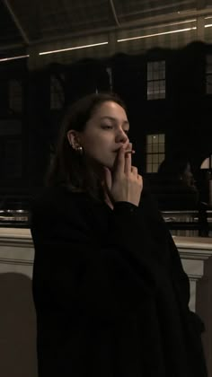 a woman standing in front of a window with her hands to her mouth and looking off into the distance