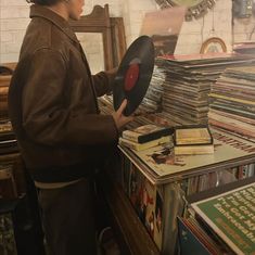 a woman holding a record in front of a table full of records and cds on it