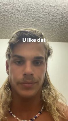 a man with long blonde hair wearing a necklace that says u like dat on it